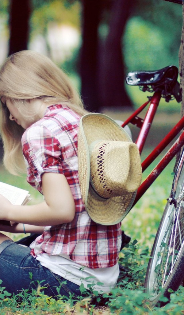 Девушка читает книгу сидя в парке на газоне