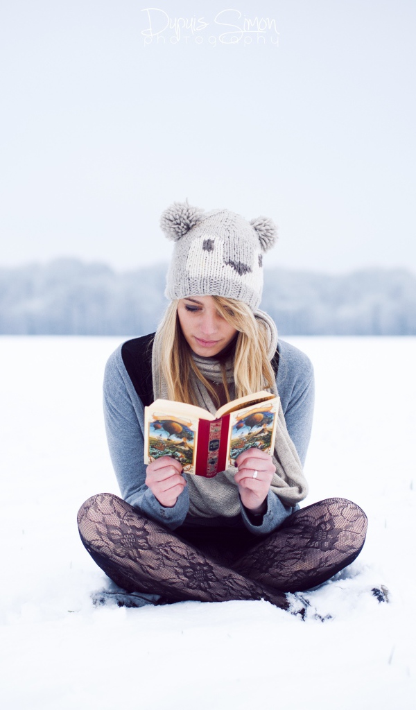 Девушка читает книгу сидя на снегу