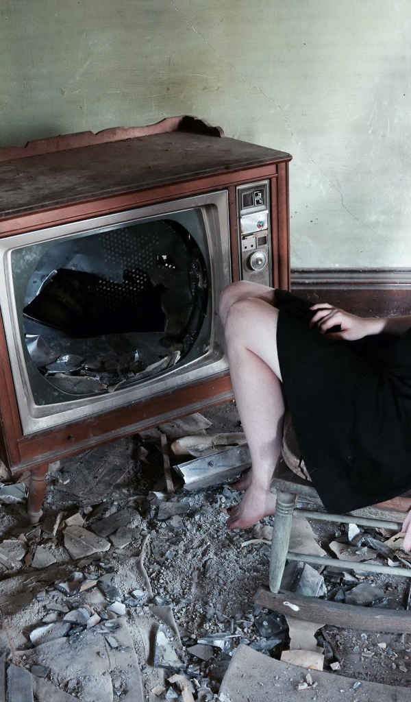 Девушка сидит у разбитого старого телевизора