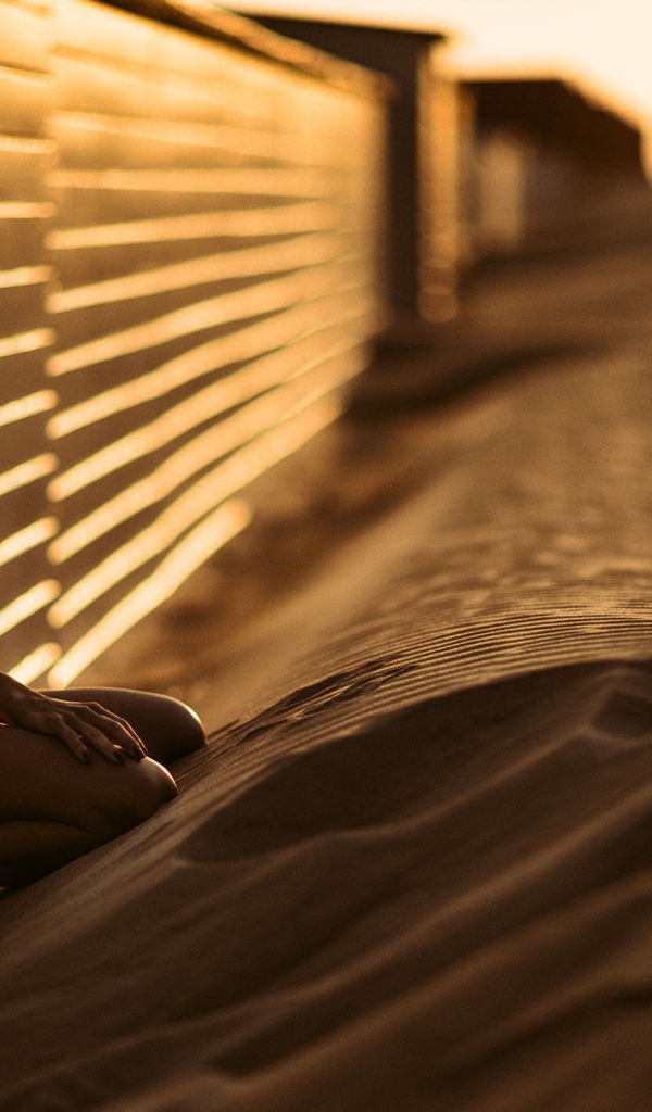 Девушка сидит на песке у забора