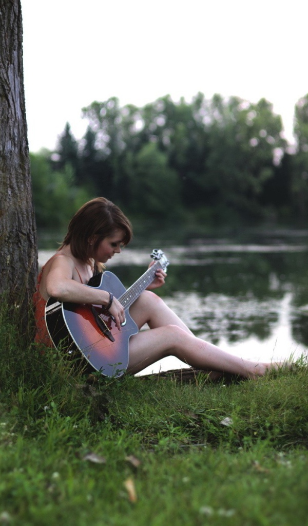 Девушка сидит  с гитарой на берегу реки