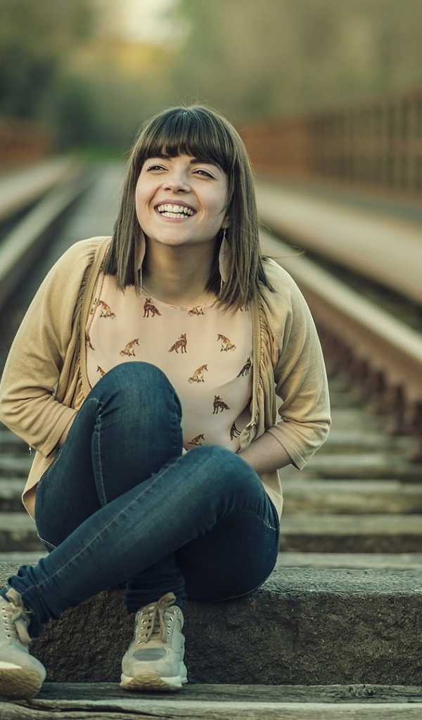 Девушка улыбается сидя на рельсах