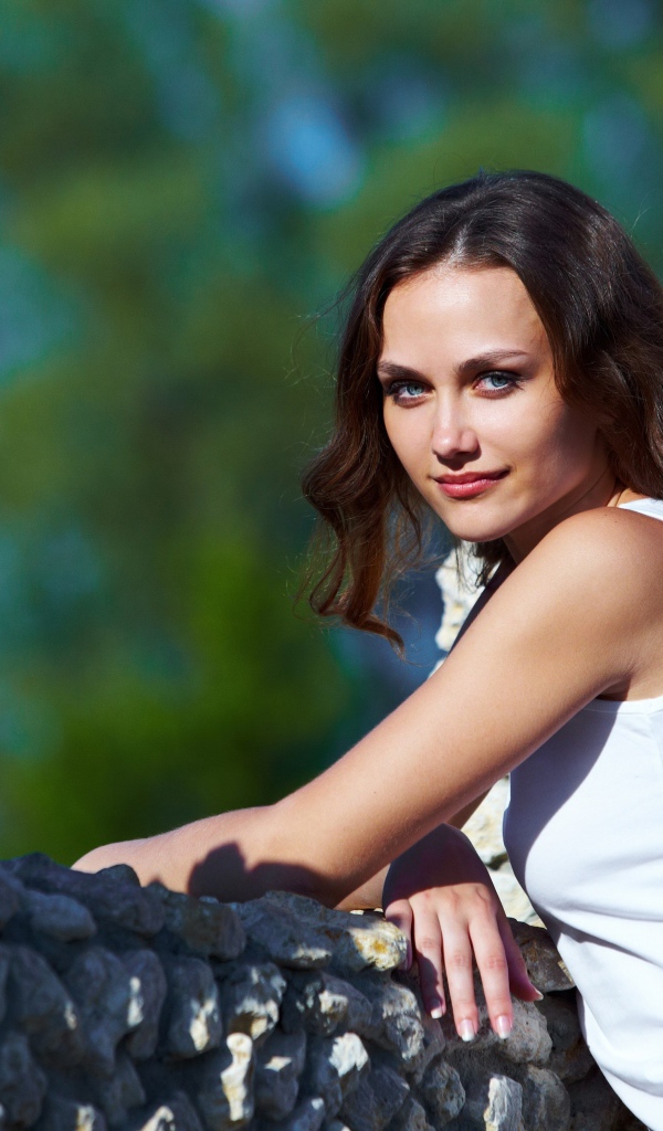 Девушка стоит у забора из камня