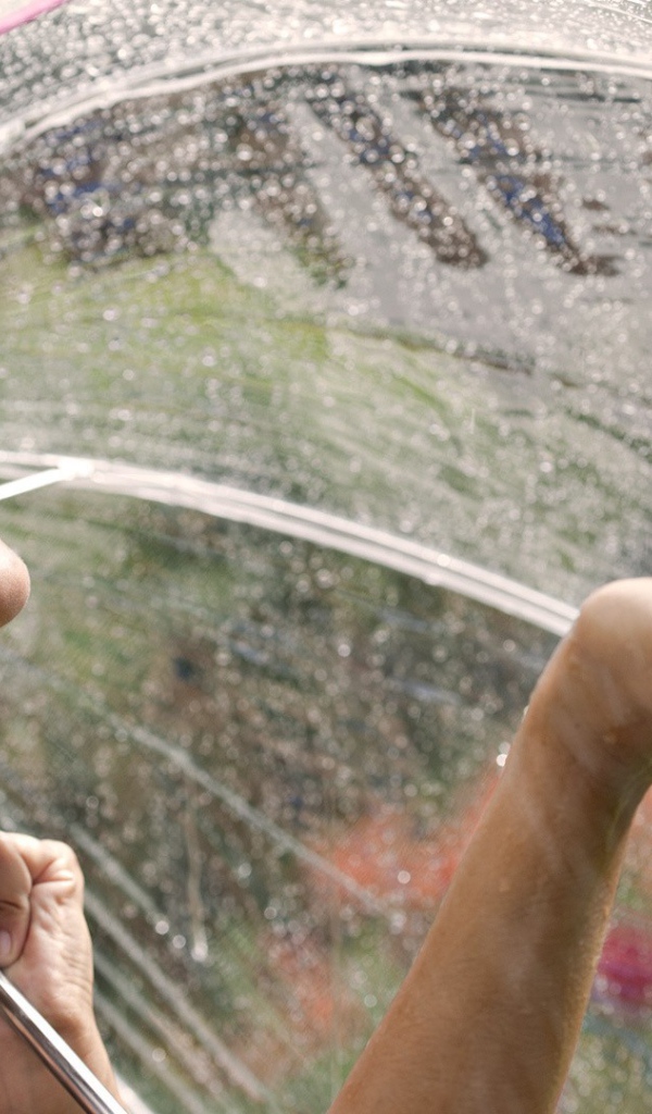 Девушка под прозрачным зонтом ловит дождь рукой