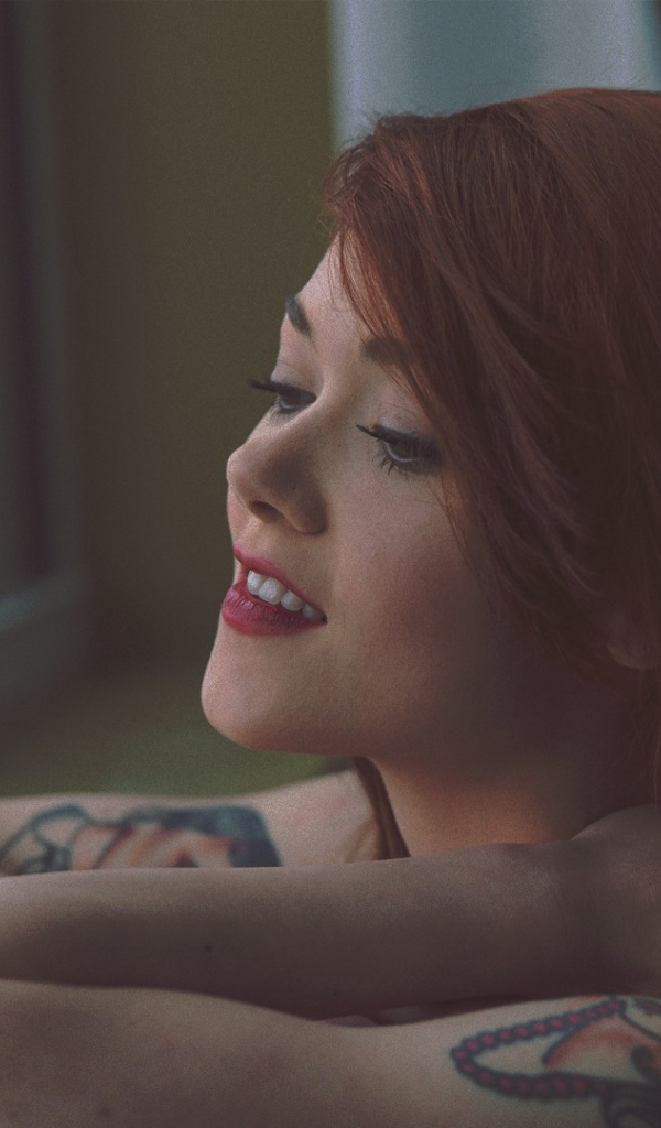 Девушка с татуировками смотрит в окно