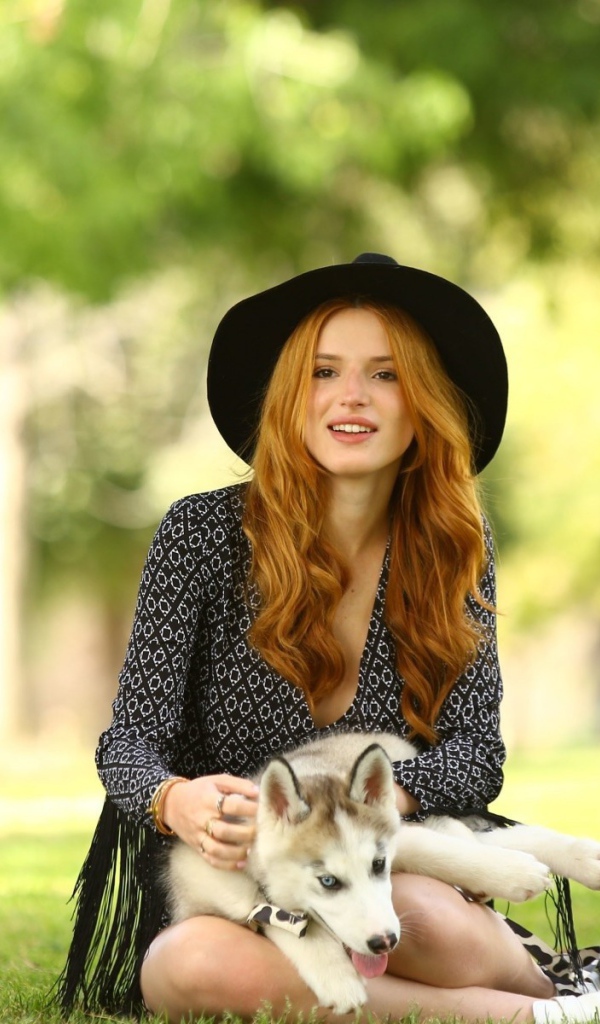Рыжеволосая девушка в шляпе ласкает щенка хаски
