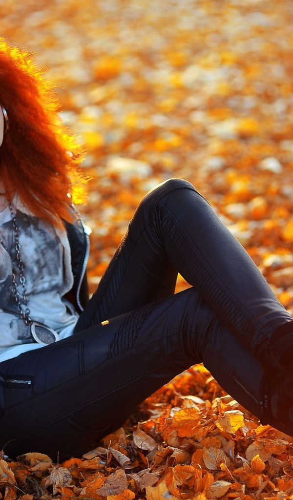 Рыжая девушка сидит на ковре из желтых листьев