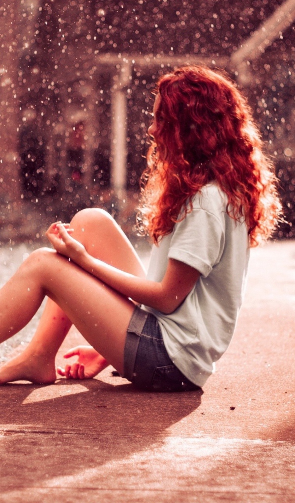 Рыжая девушка сидит на земле во время дождя