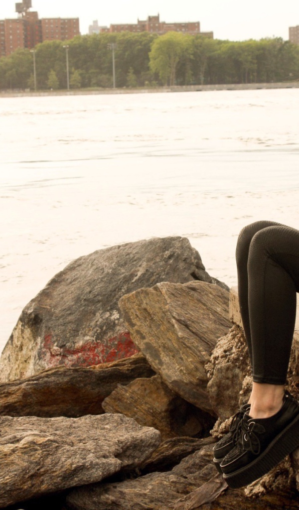 Рыжая девушка сидит на плитах набережной