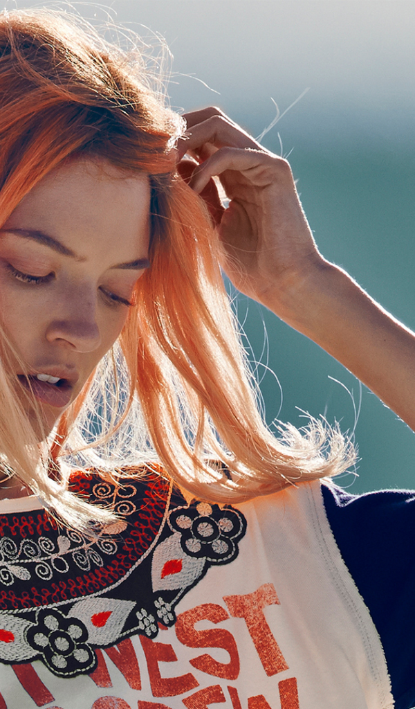 Рыжая девушка на ветру поправляет волосы