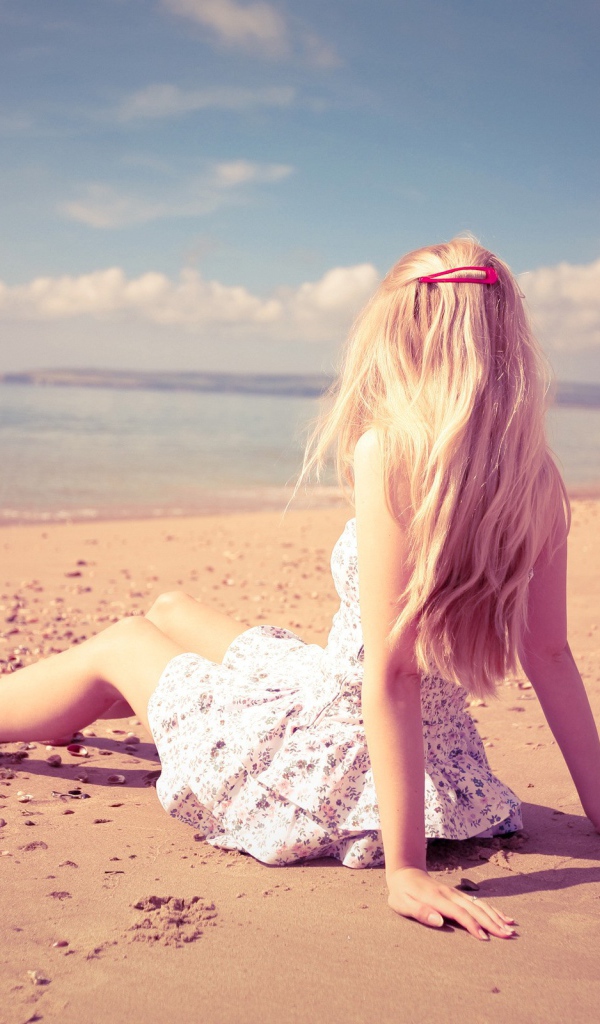 Блондинка с розовой заколкой сидит на пляже