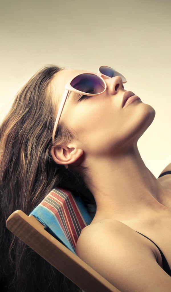 Девушка в очках загорает в шезлонге