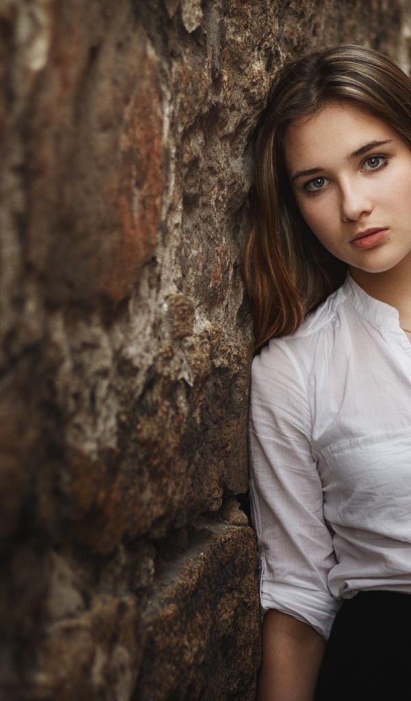 Девушка в белой рубашке стоит у стены