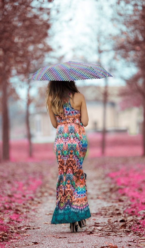 Девушка под зонтом в красивом платье идет по аллее