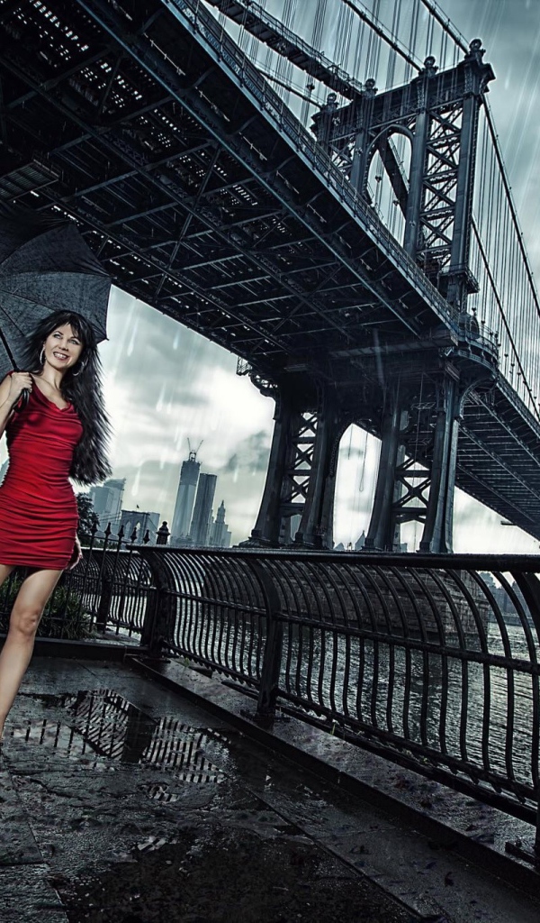 Модель в красном платье с зонтом стоит под мостом