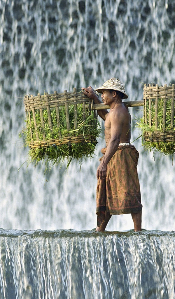 Крестьянин с корзинами идет по водопаду