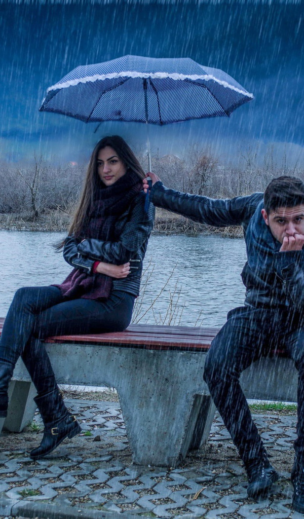 Парень держит над девушкой зонт во время дождя