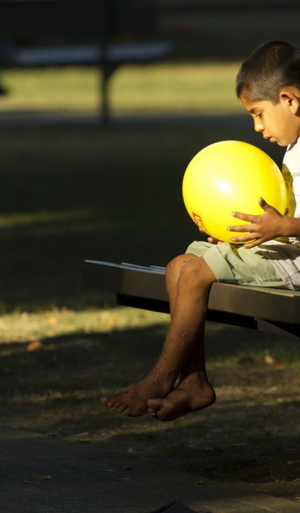 Мальчик сидит на скамье с шариком в руках