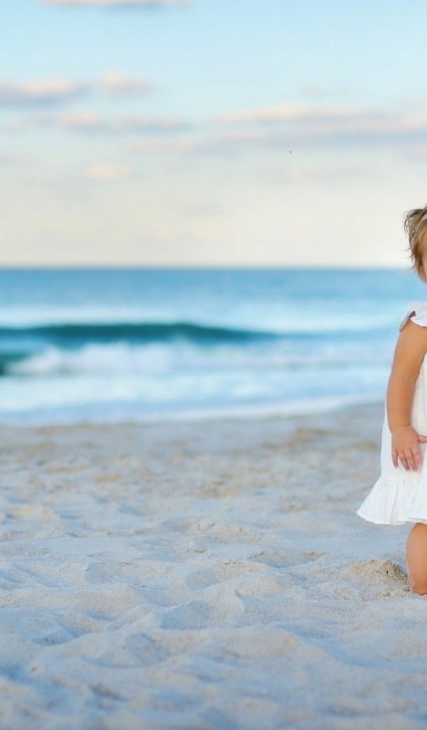 Девочка в белом платье на песке пляжа