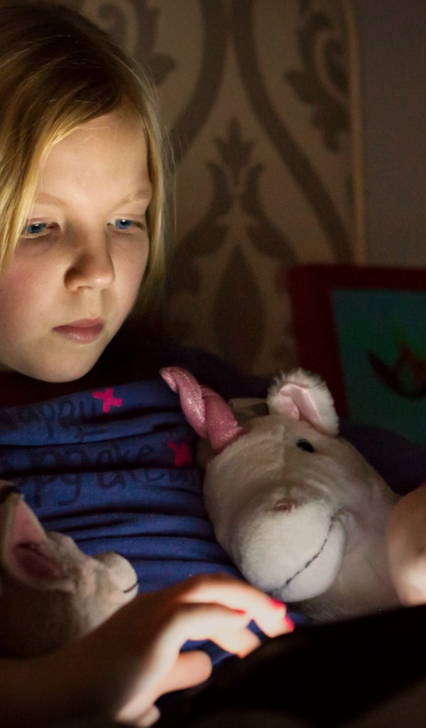 Девочка играет с планшетом лежа в кровати