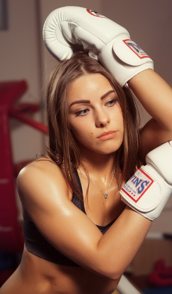 Девушка в белых перчатках отдыхает у канатов ринга