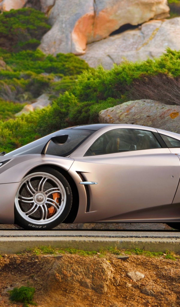 Серебристый быстрый автомобиль  Pagani Huayra на трассе у скалы