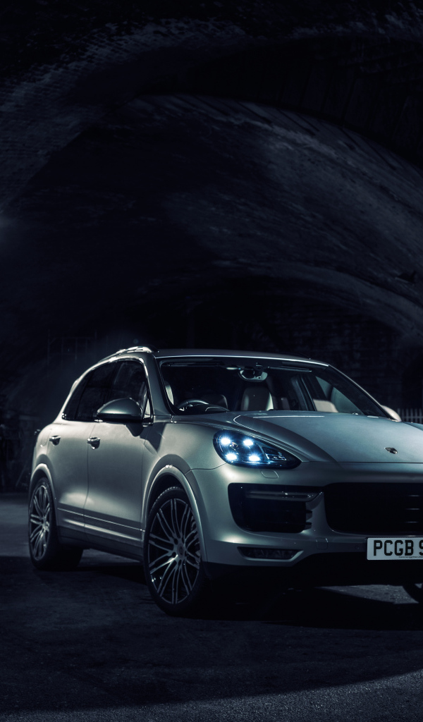 Серебристый автомобиль Porsche Cayenne в тоннеле с включенными фарами