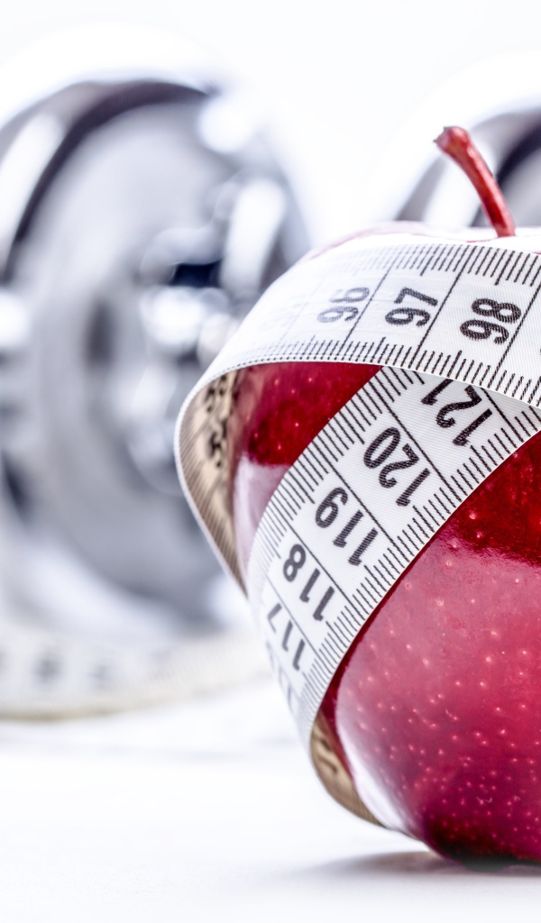 Красное яблоко перемотано мерной лентой и гантели на белом фоне