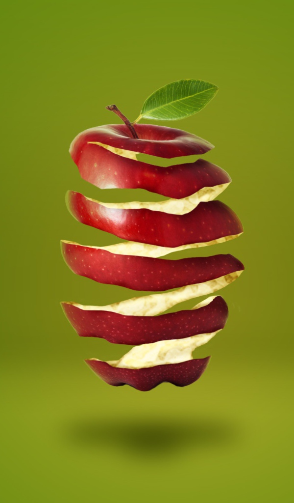 Нарезанное спиралью красное яблоко на зеленом фоне 