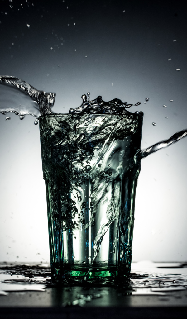Брызги воды из стакана с водой на сером фоне