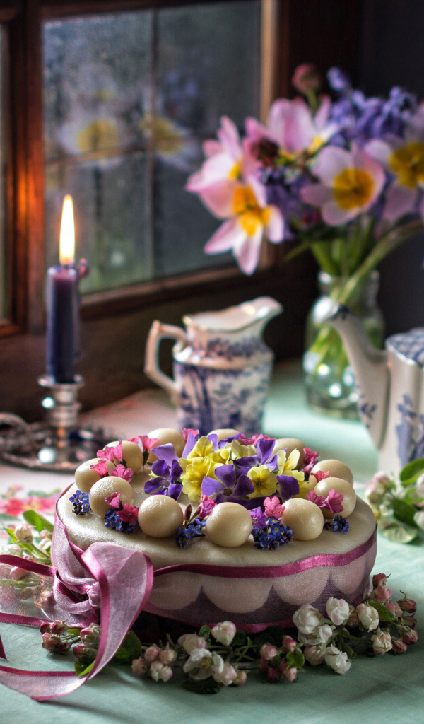 Красивый торт на столе с сервизом и горящей свечой у окна