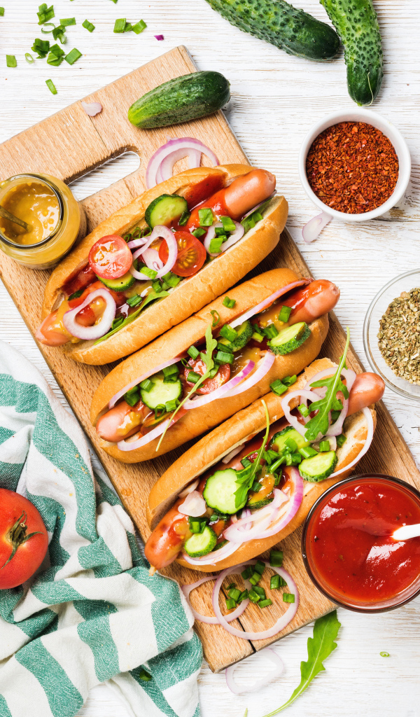 Аппетитные хотдоги на разделочной доске с овощами