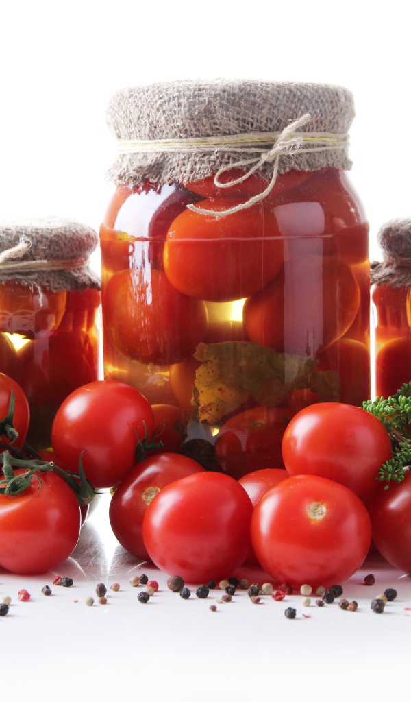 Банки с консервированными и свежими помидорами на столе со специями на белом фоне