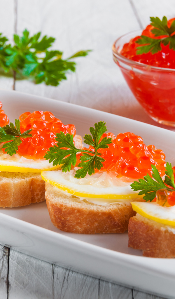 Бутырброды с красной икрой и лимонами на белой тарелке