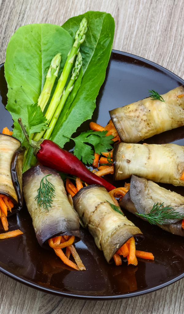 Рулетики из баклажанов с морковью на тарелке с листьями салата