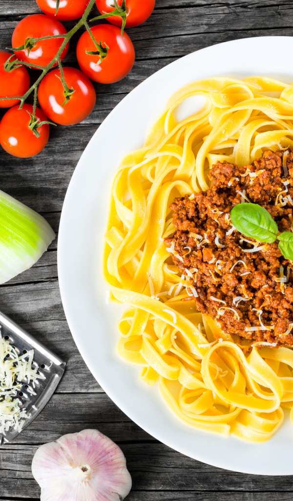 Спагетти на белой тарелке с мясом и сыром