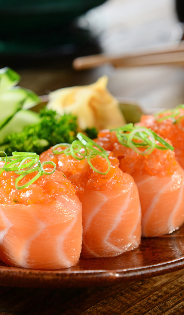 Суши из красной рыбы на тарелке со свежими огурцами и зеленью