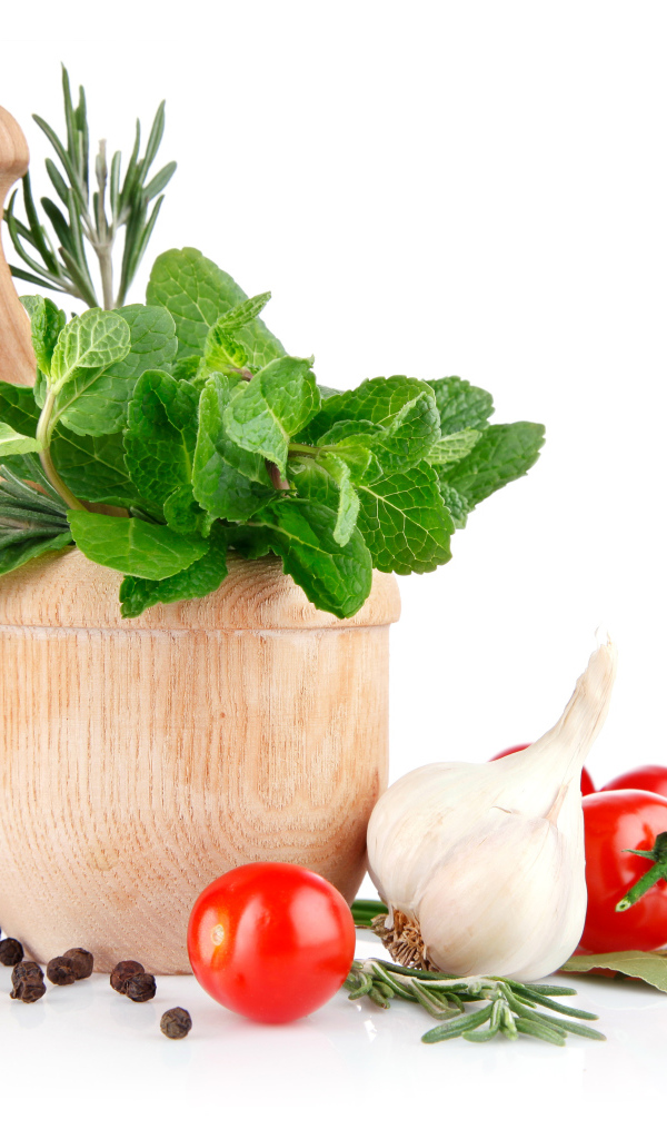 Деревянная ступа и пестик со специями и зеленью на столе с чесноком и помидорами