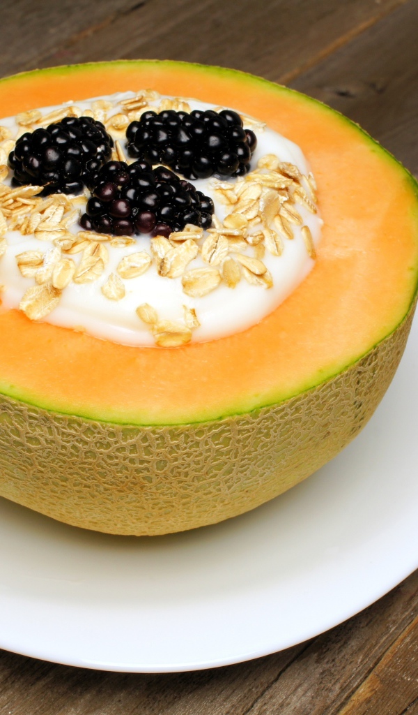 Йогурт с ежевикой и овсянкой в тарелке из свежей дыни на завтрак