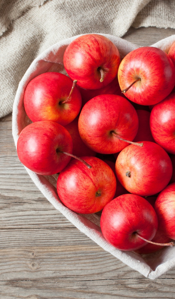 Красивые красные яблоки в тарелке в форме сердца на столе