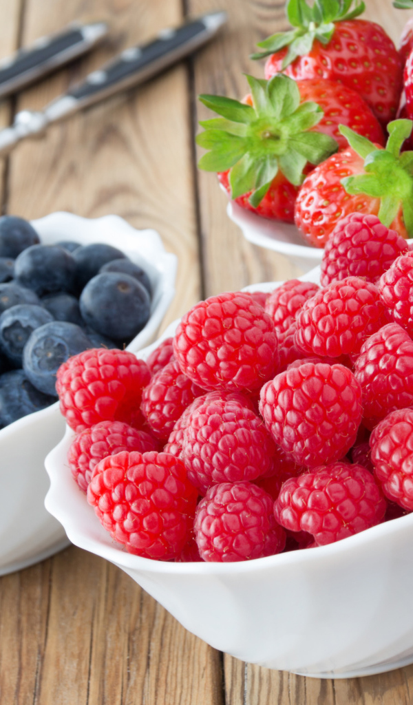 Свежие ягоды малины, клубники и черники в белых тарелках на столе