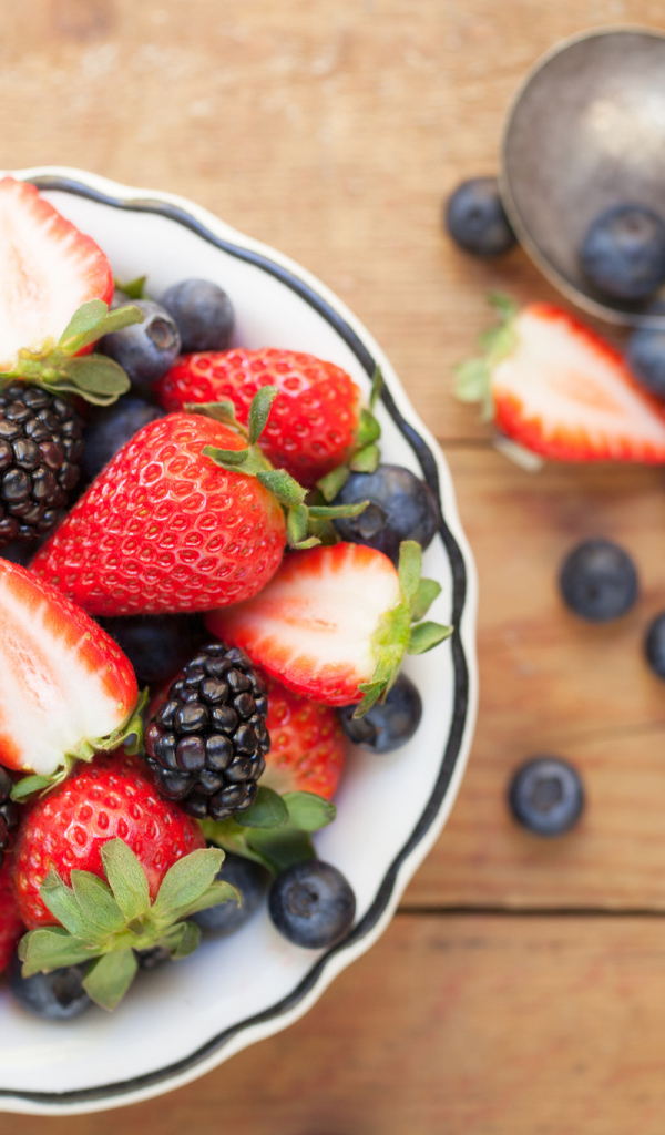 Свежие ягоды клубники, черники и ежевики в тарелке на деревянном столе