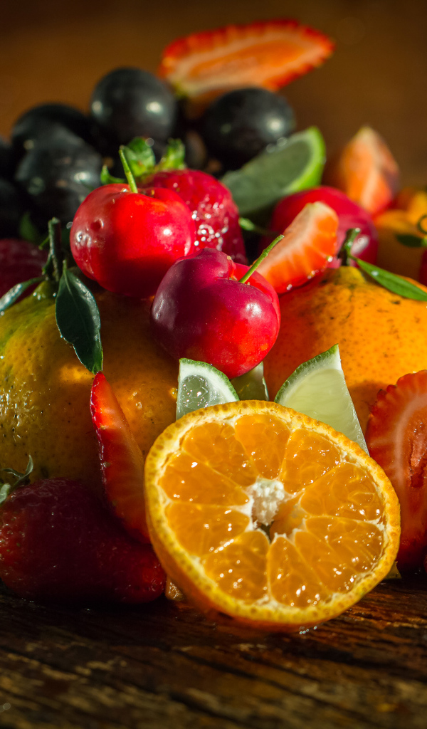 Свежие кусочки апельсина, лимона и ягоды вишни и клубники на столе