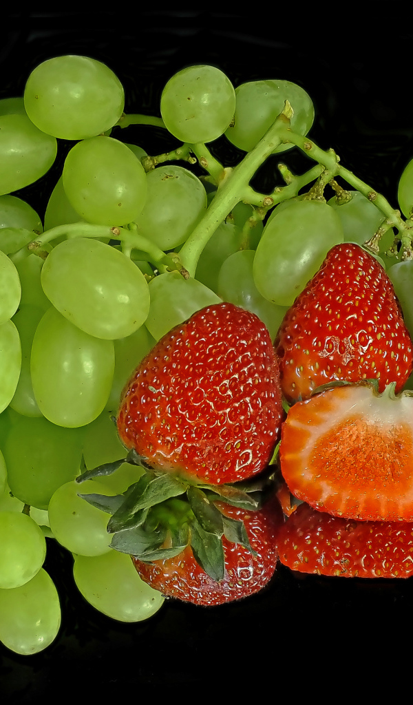 Зеленый виноград и спелая клубника на черном фоне 