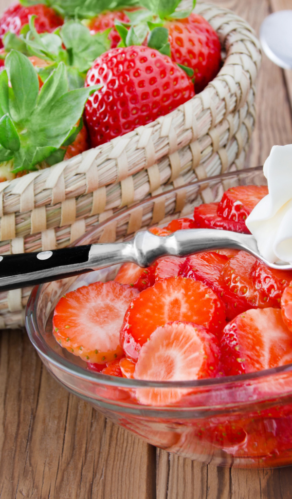 Нарезанная клубника в стеклянной посуде с ложкой сливок