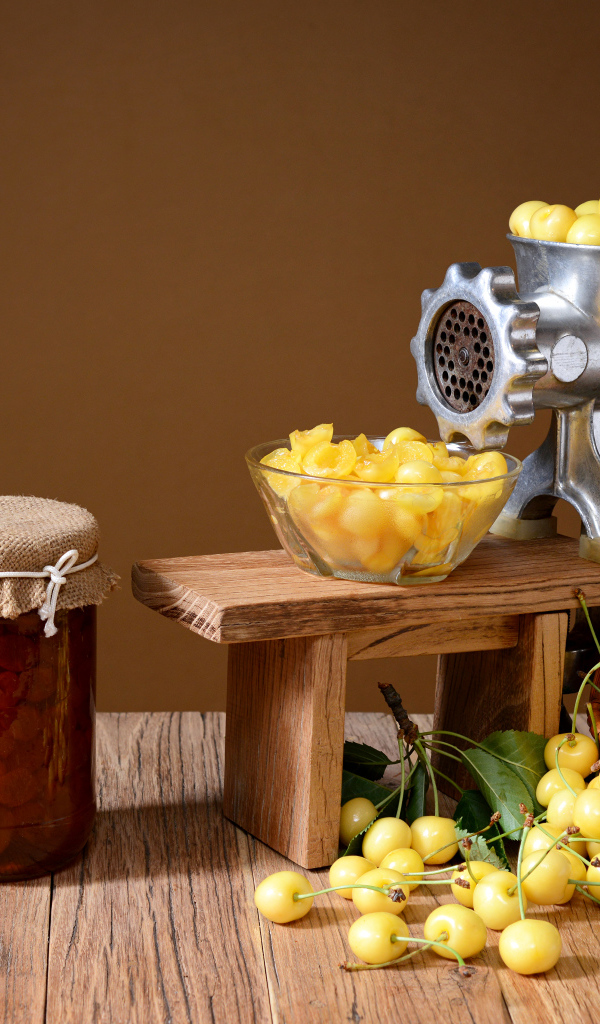 Две баночки варенья и желтые черешни на столе с мясорубкой