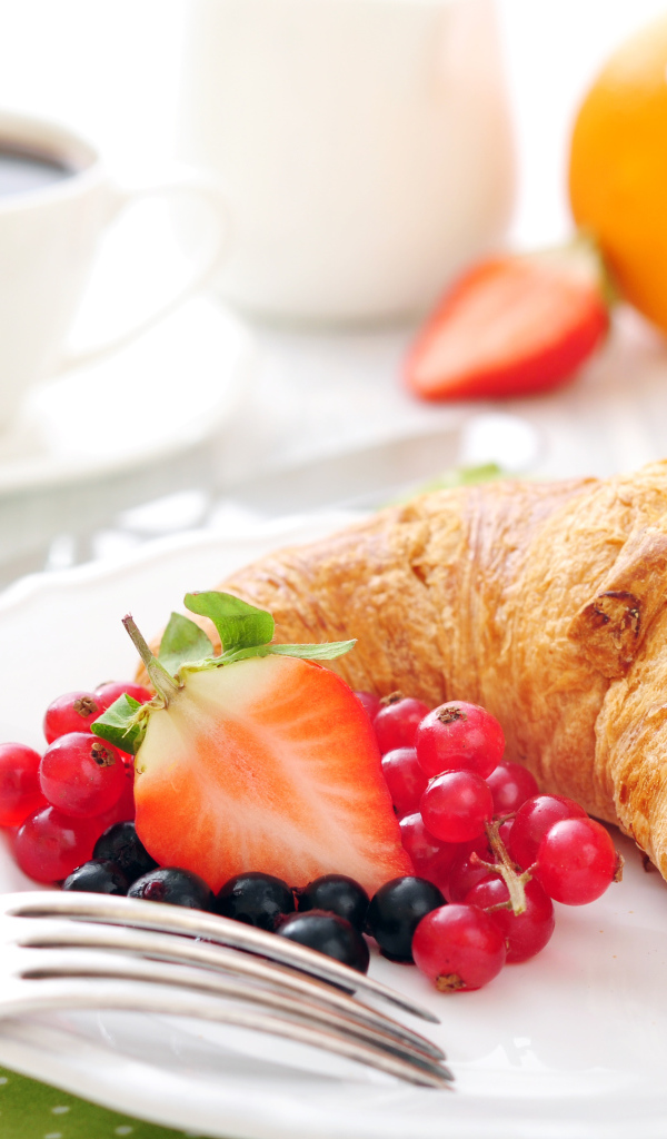 Свежий круассан на белой тарелке с ягодами 