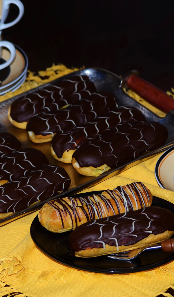 Аппетитные сладкие эклеры с шоколадом и чашками кофе на столе