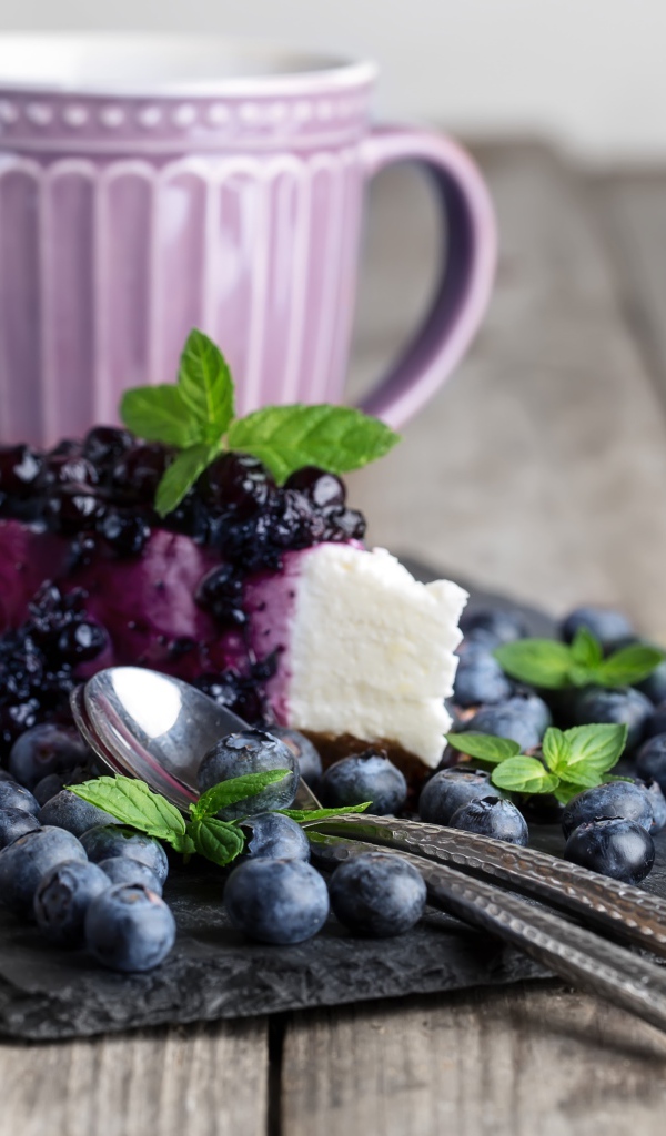 Черничный чизкейк со свежими ягодами лежит на столе с чашкой