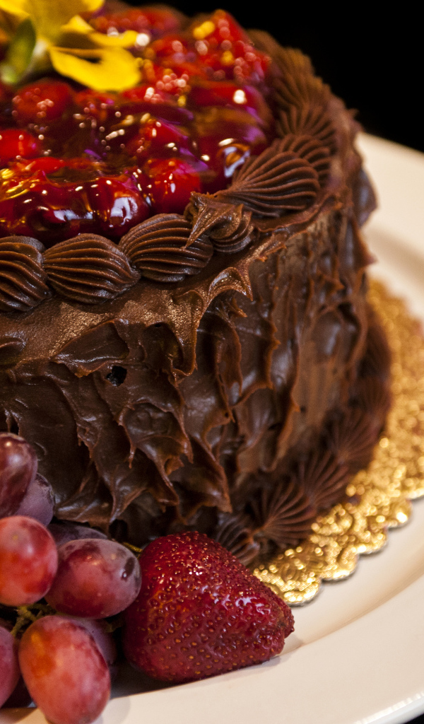 Торт с шоколадным кремом, виноградом и клубникой на белой тарелке